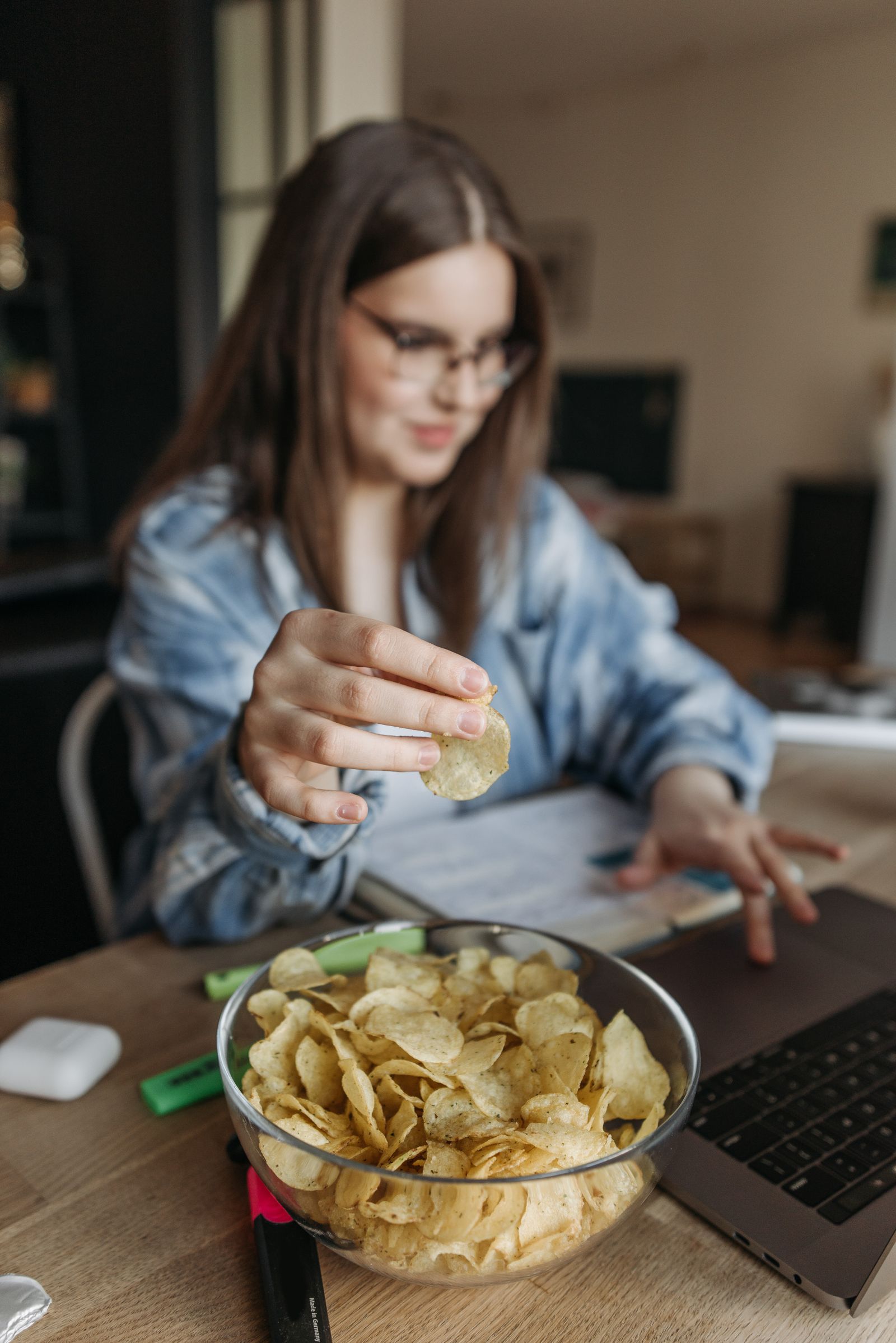 Photo: Pavel Danilyuk / Pexels A woman snacking from a bowl of potato chips while working at a laptop